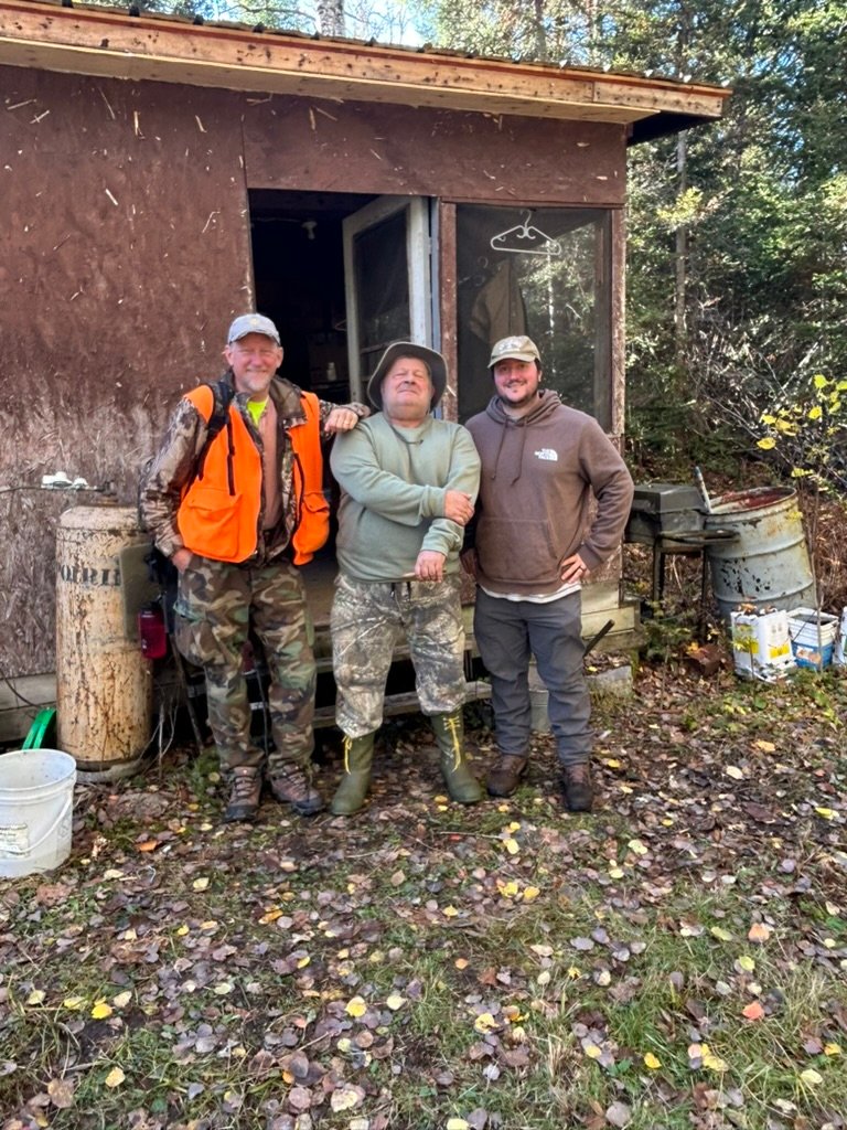 Robby with his dad and a friend standing in front of the moose camp cabin