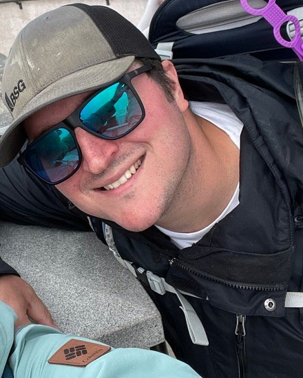 Robby smiling in a ball cap and sunglasses while hiking